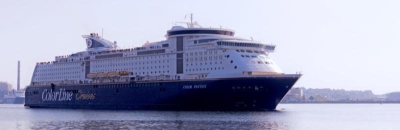 De Color Fantasy van Color Line vaart bij vlak water een haven uit, een donkerblauwe romp met het opschrift Color Line Cruises en daarboven een hoog wit dekkenhuis met balkons