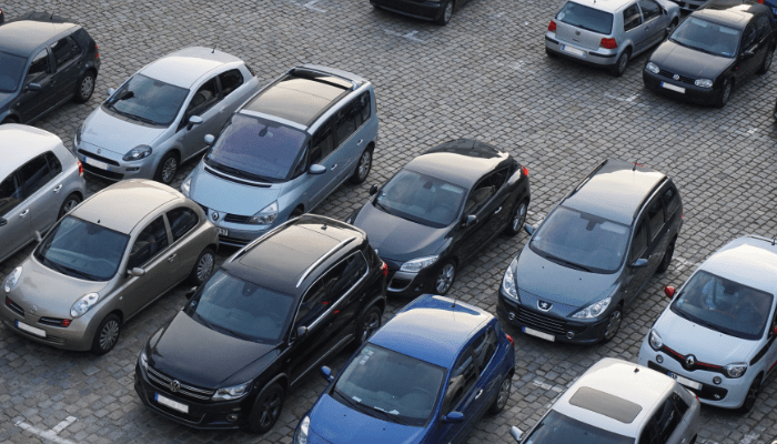Een vol parkeerterrein van bovenaf gezien, met personenauto’s in schuine vakken op een bestrating van kinderkopjes