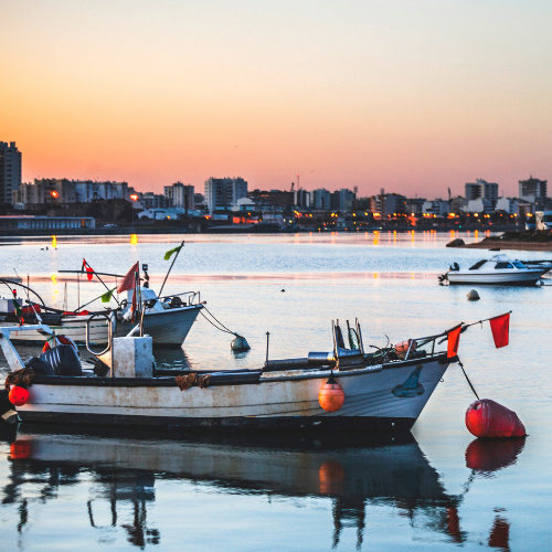 Vissersbootjes in de rivierhaven van Portimão bij zonsondergang, met de stad op de achtergrond