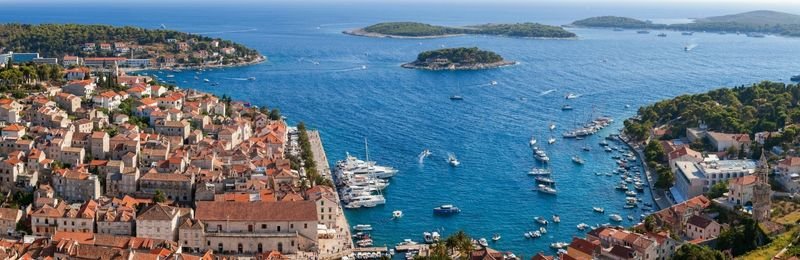 Uitzicht over de daken van Hvar-stad op een baai vol boten, met de beboste Pakleni-eilanden in zee