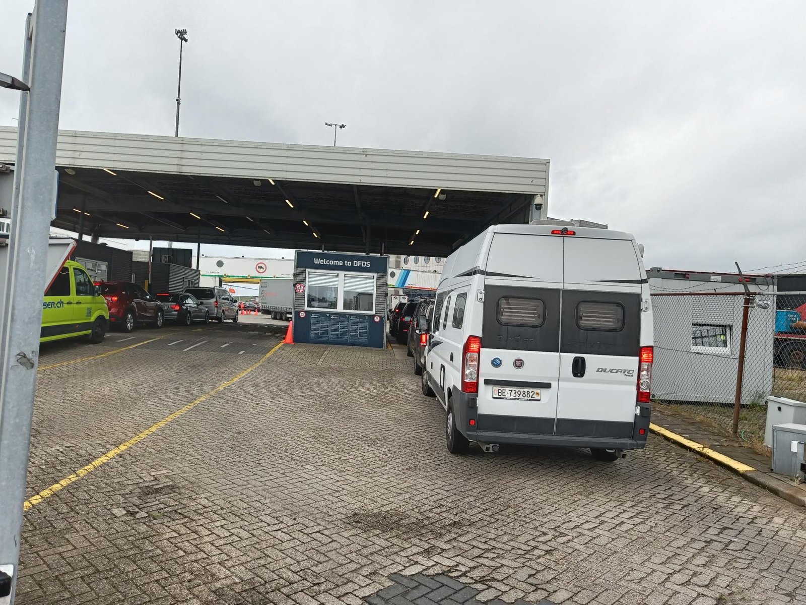 Auto's en een camper in de rij voor de controlepost onder de overkapping in IJmuiden, met 'Welcome to DFDS' op het hokje