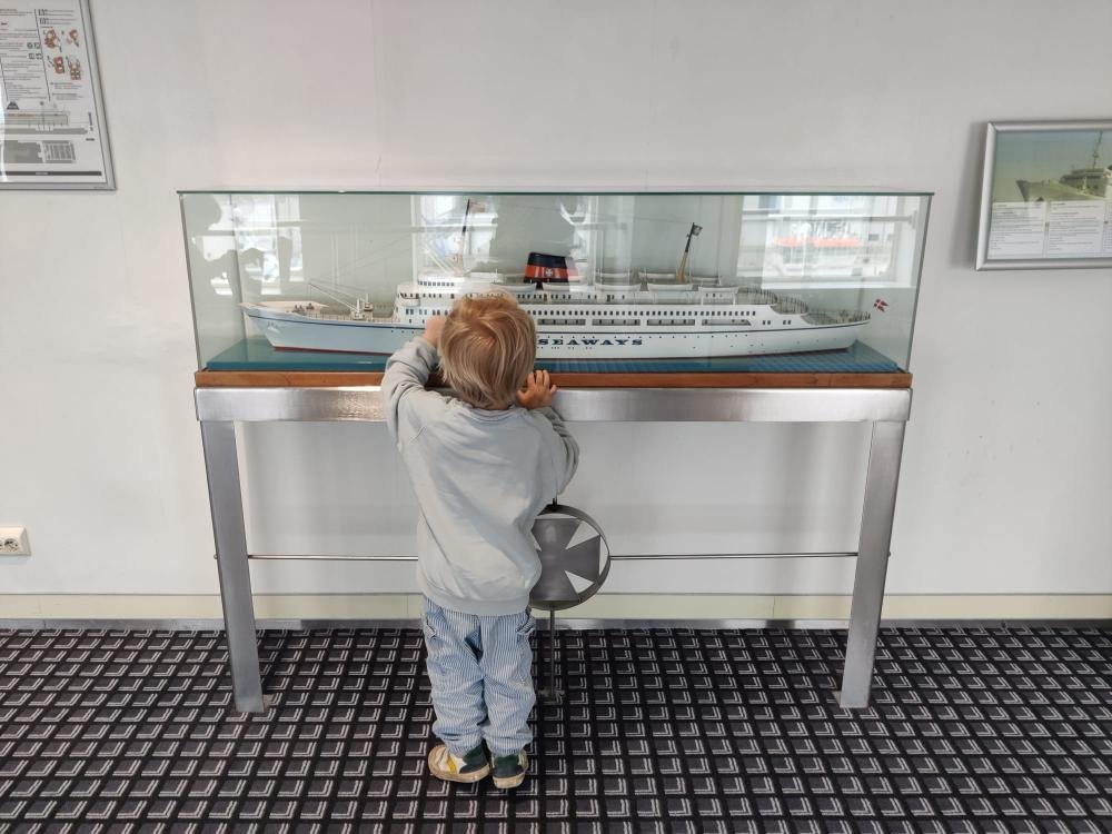Een klein kind kijkt in een vitrine met een schaalmodel van een ouder Seaways-schip aan boord