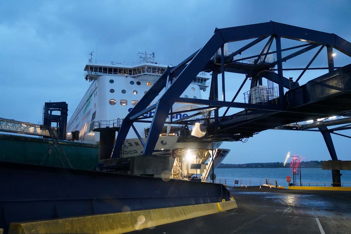 De veerboot aan de aanlegbrug in Harwich bij schemer, met de verlichte opening in de boeg en een rood verkeerslicht op de kade