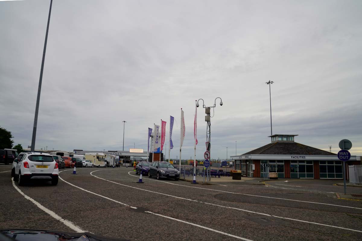 Auto's in de rij op het opstelterrein van Harwich International, met de vlaggen van Stena Line en een laag gebouw met het opschrift Facilities