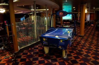 Airhockey tafel aan boord bij P&O Ferries met op de achtergrond de bovenste verdieping van de Show Bar en een videoscherm waarop voetbal wordt vertoond.