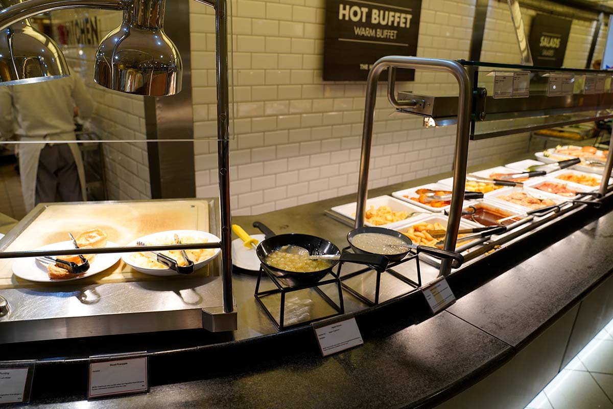 De buffetlijn aan boord onder het bord Hot Buffet, met warmhoudlampen en nog enkele schalen eten