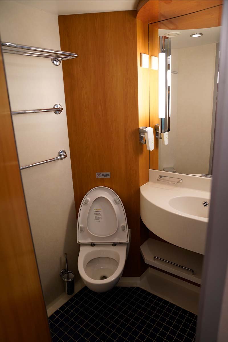Kleine badkamer in een hut met een hangtoilet, een hoekwastafel met spiegel en drie handdoekstangen aan de wand