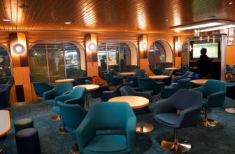 Blauwe stoelen in een lounge aan boord van de Hoek van Holland - Harwich veerboot, waar een man op een PlayStation 5 aan het spelen is.