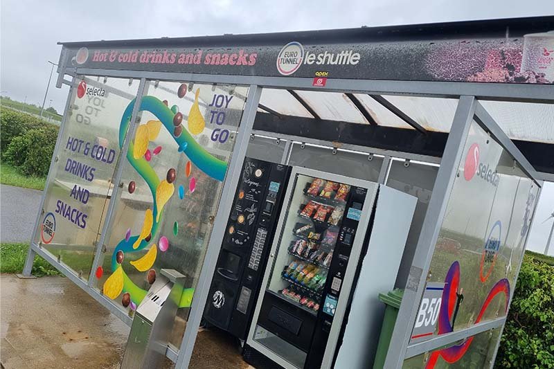 Glazen hokje op het opstelterrein met een snackautomaat en een koffieautomaat, met erboven de tekst hot and cold drinks and snacks