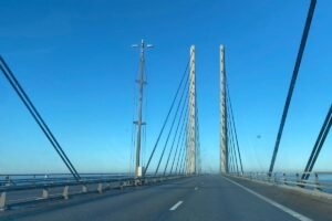 De rijbaan van de Sontbrug gezien vanuit de auto, met de twee betonnen pylonen en hun tuikabels tegen een strakblauwe lucht