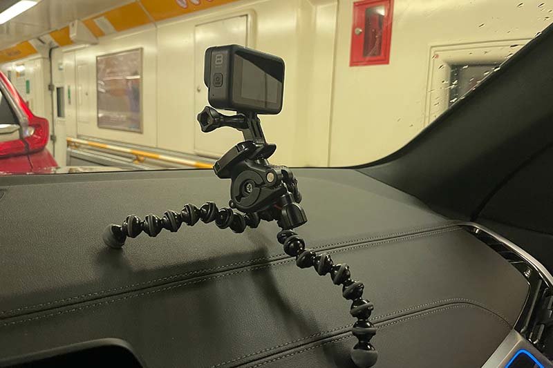 Actiecamera op een flexibel statief op het dashboard van de auto, met door de voorruit de witte wand van de treinwagon