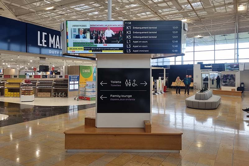 Vertrekbord in de terminal met treinnummers K1 tot L5 en de meldingen embarquement terminé en appel en cours, naast een duty-freewinkel