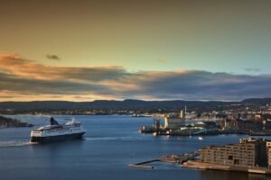 Een veerboot in de vroegere blauw-witte DFDS-kleuren vaart bij zonsondergang de haven van Oslo uit, met de stad en de heuvels op de achtergrond