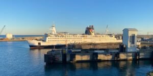 Een witte veerboot van Scandlines aan de kade in een haven, in laag winterlicht onder een strakblauwe lucht, met een kademuur en een grijze liftkoker op de voorgrond