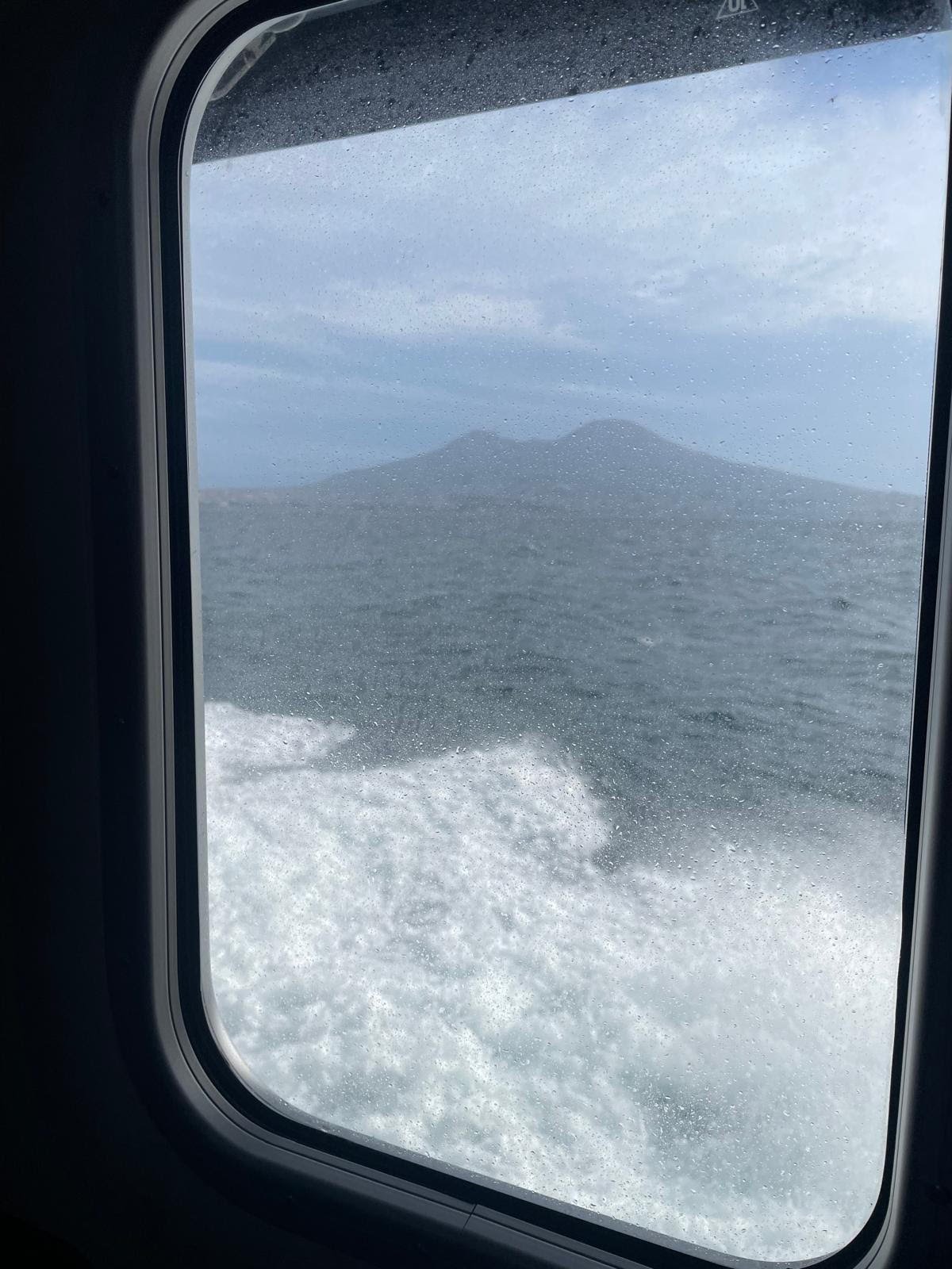 De Vesuvius gezien door een nat raam van de draagvleugelboot, met het schuim van de zee eronder
