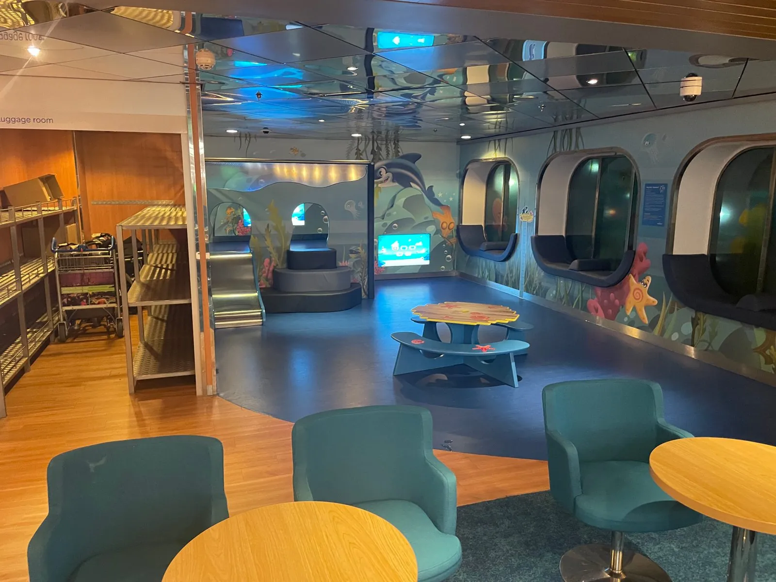Speelhoek voor kinderen met een onderwaterschildering, een glijbaan en zitnissen met schermen; links ernaast een bagageruimte met rekken