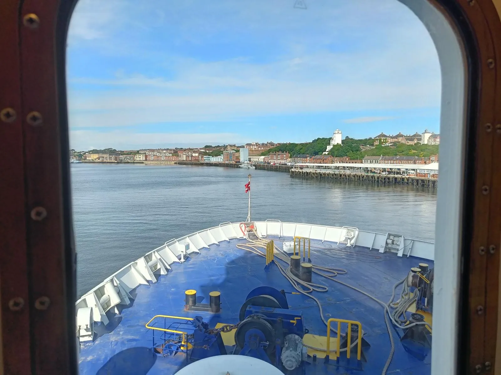Uitzicht door het hutraam over de blauwe boeg, varend over de Tyne langs de kade van North Shields