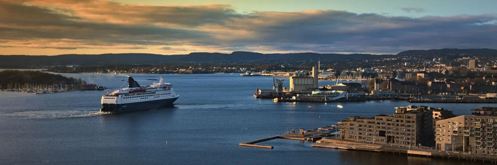 Een veerboot vaart bij zonsondergang de Oslofjord op, met de stad rechts