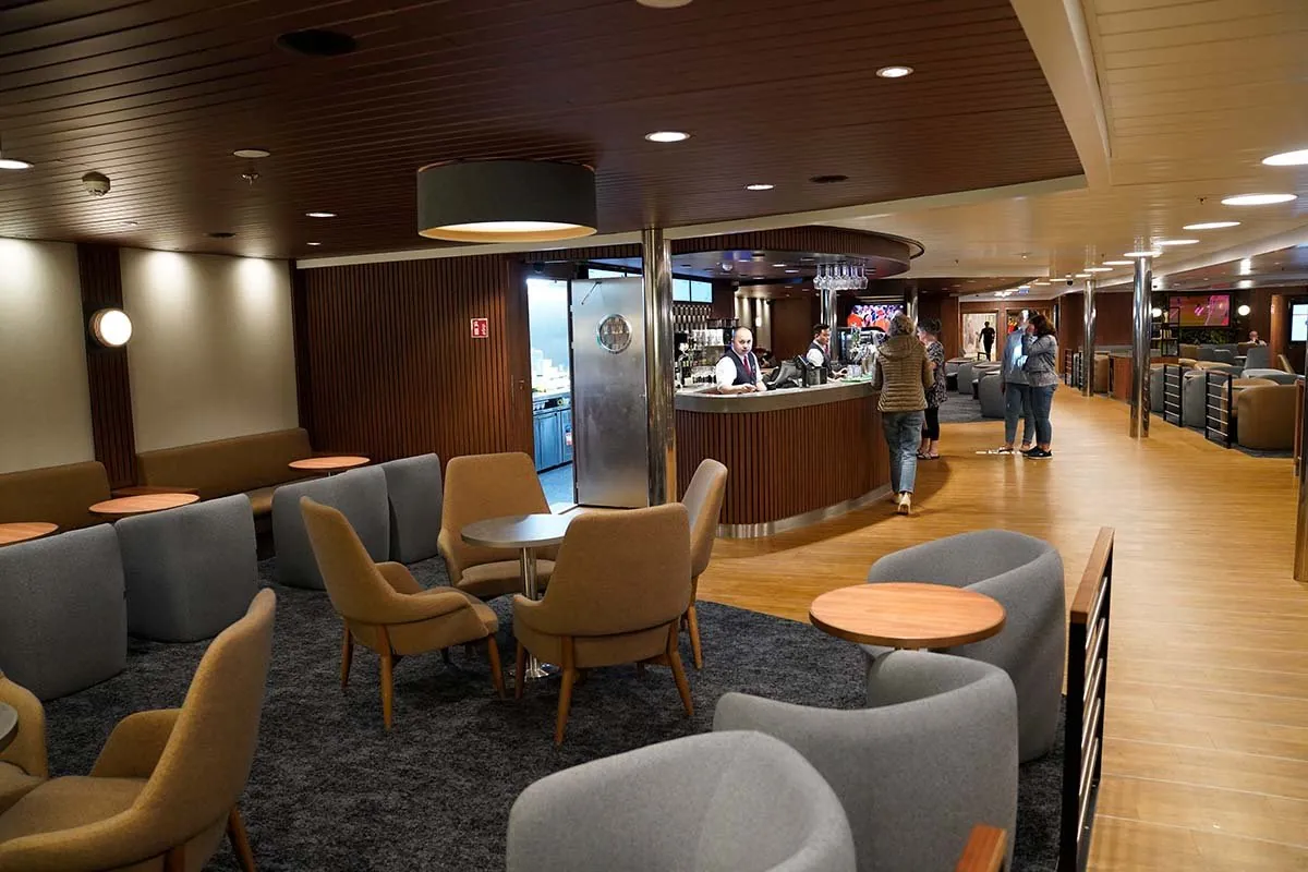De bar aan boord met een gebogen toog, een barman erachter en fauteuils eromheen