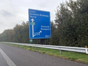 Een blauw bord langs de E40 in België met Calais, Duinkerke (Dunkerque) en Veurne rechtdoor, en Diksmuide en Nieuwpoort bij de afslag naar de N355