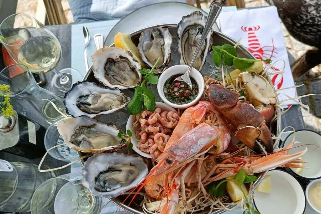 Een schaal met oesters, garnalen en een krab op een terrastafel, met twee glazen witte wijn ernaast