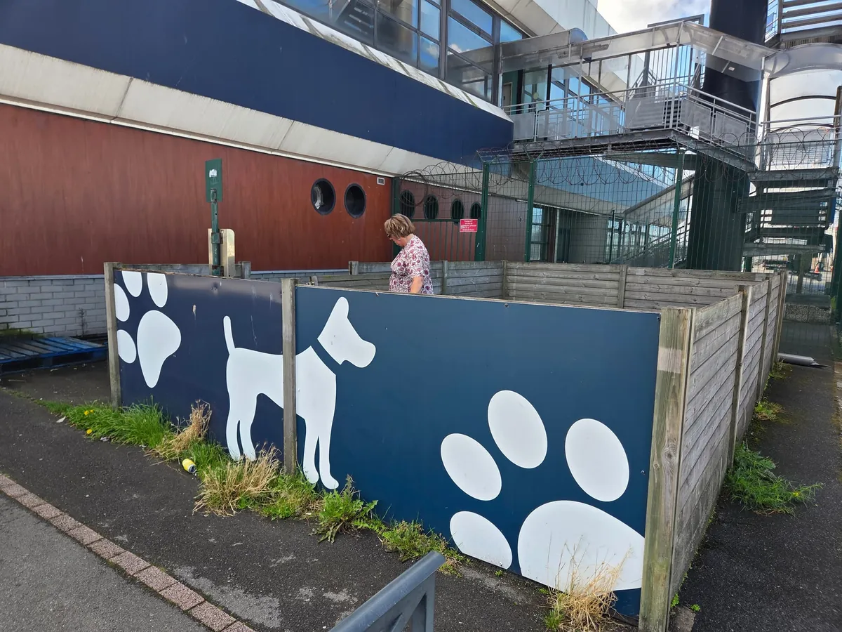 Een omheind hondenveldje met pootafdrukken en een hondensilhouet op de schutting, bij de DFDS-terminal