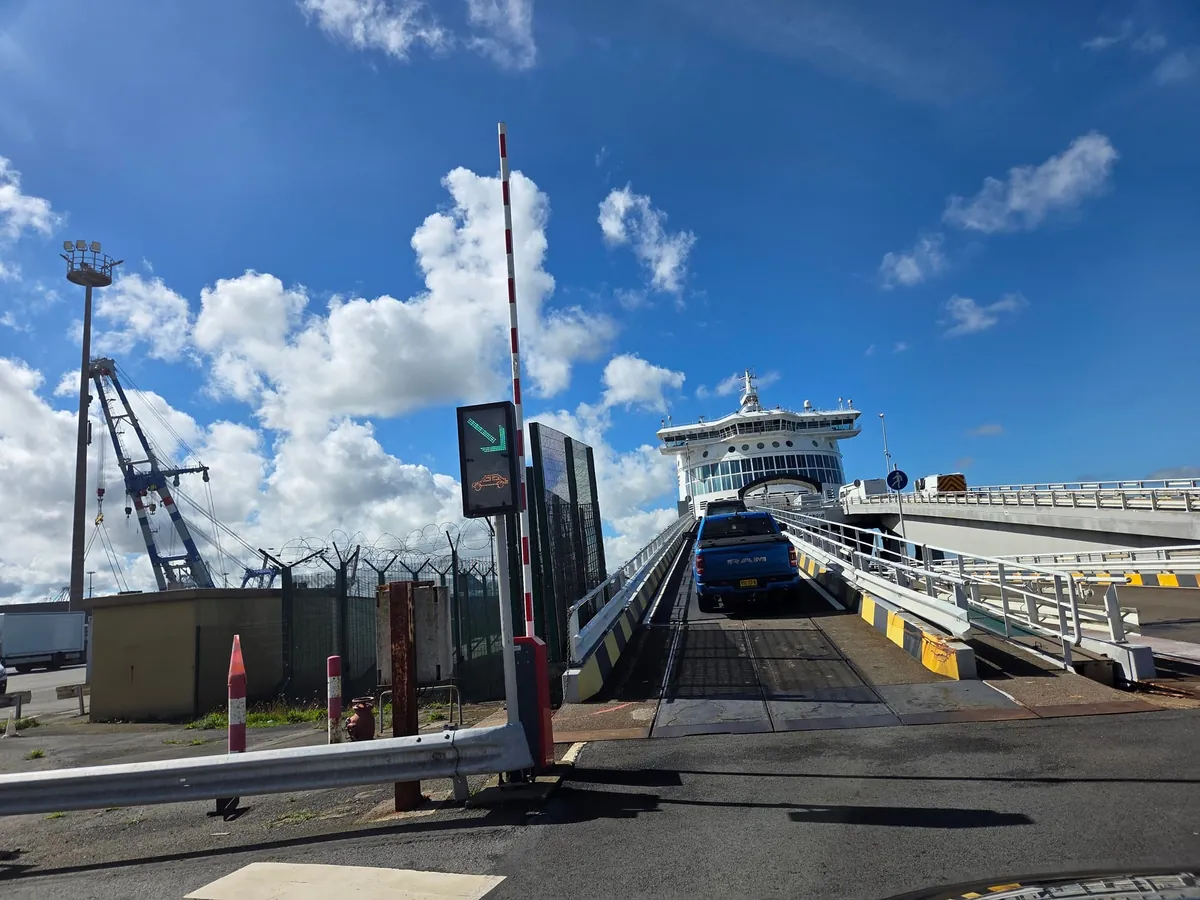 Een auto rijdt over de oprit de DFDS-veerboot op in de haven van Duinkerken, met een slagboom en een kraan ernaast