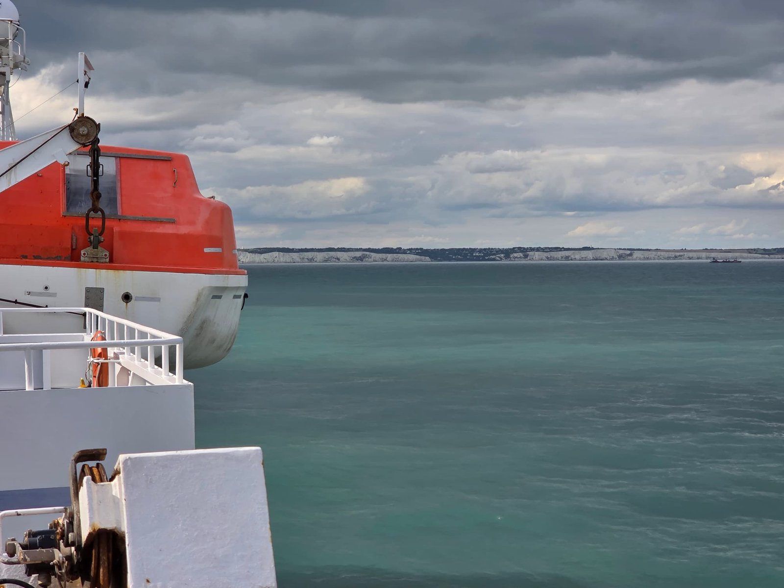 Een oranje reddingsboot met roest aan de reling van de Delft Seaways, met de witte kliffen van de Engelse kust in de verte