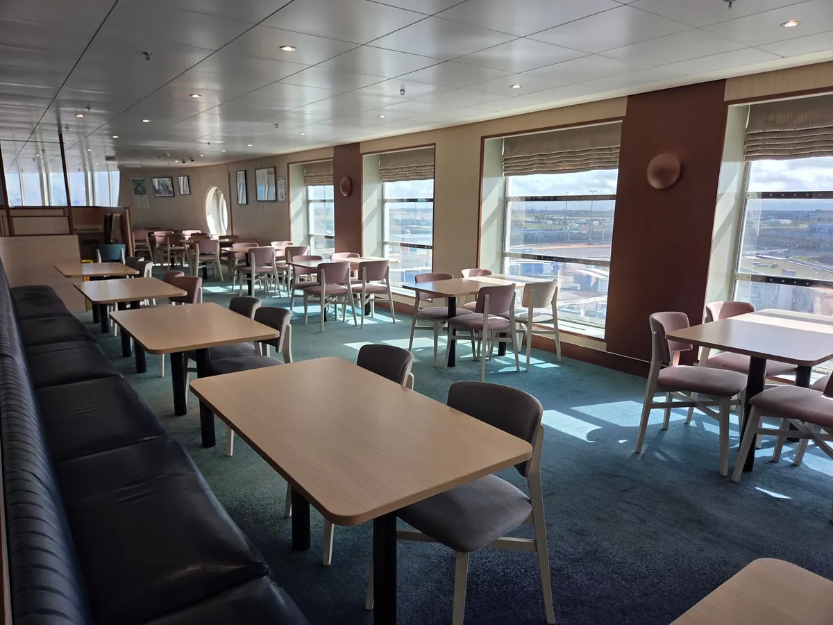 Een restaurant met houten tafels, stoelen en grote ramen aan boord van de Delft Seaways