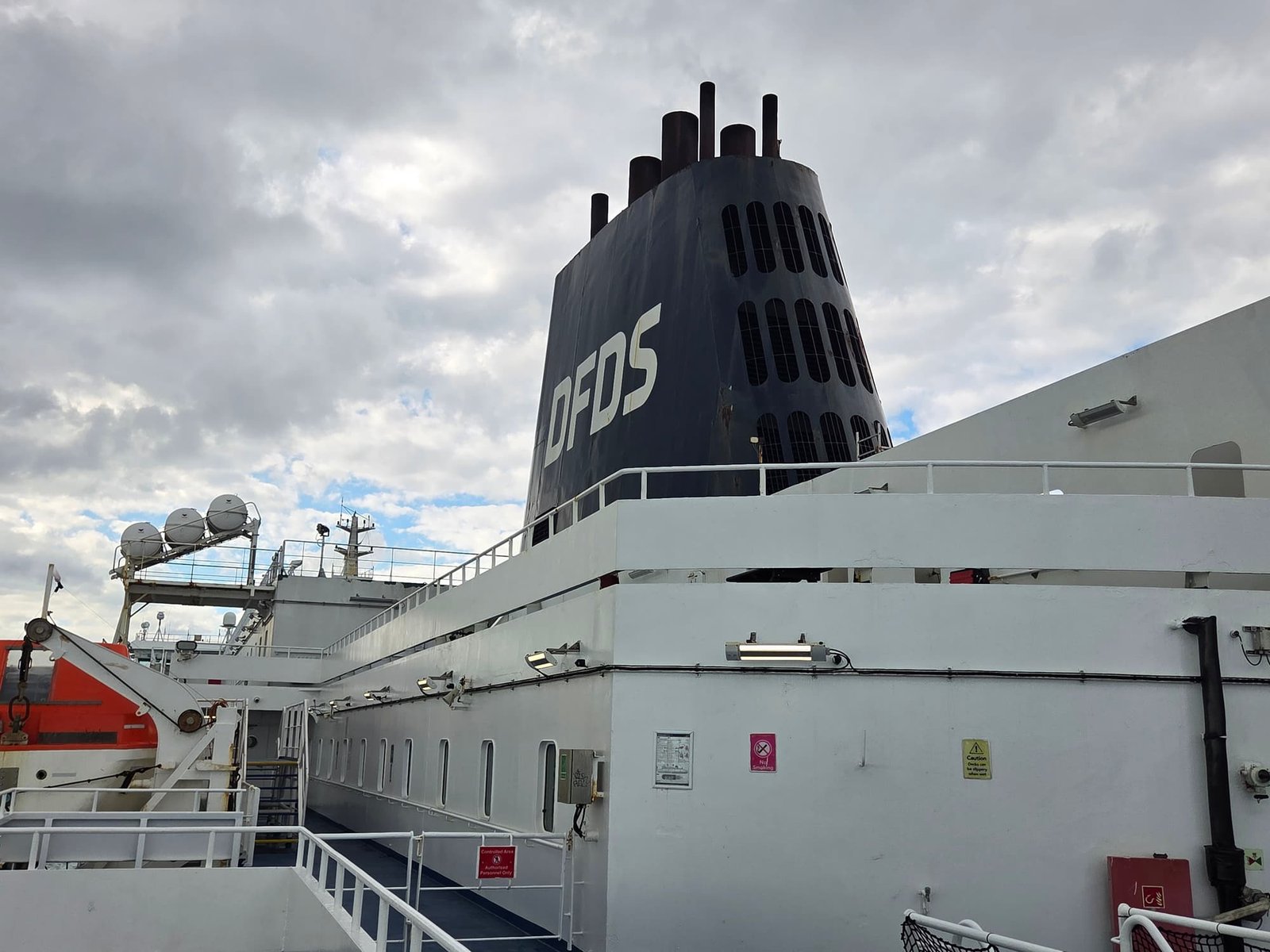 De zwarte DFDS-schoorsteen en het buitendek van de Delft Seaways onder een bewolkte lucht, met de reddingsboten ernaast
